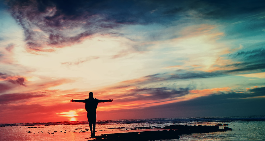 Man standing with arms open wide at the colorful horizon